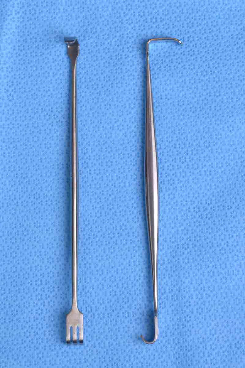 This double-ended retractor has one end that is angled and blunt.  The other end, which is directed in the opposite direction, is rake shaped with three prongs which can be either sharp or blunt. This retractor has many uses and one such example is for elevating malar tissues during a mid-face lift